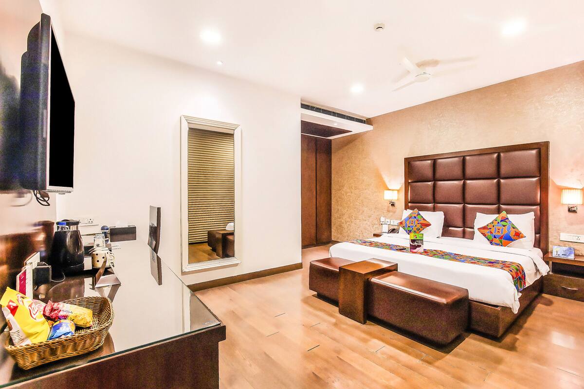Habitación de hotel con una cama grande, televisión, escritorio con cesta de aperitivos y ventana con persianas.