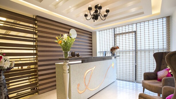Uma área de recepção com design moderno, destacando um balcão com uma letra decorativa, um lustre e um espaço de estar com uma poltrona marrom.