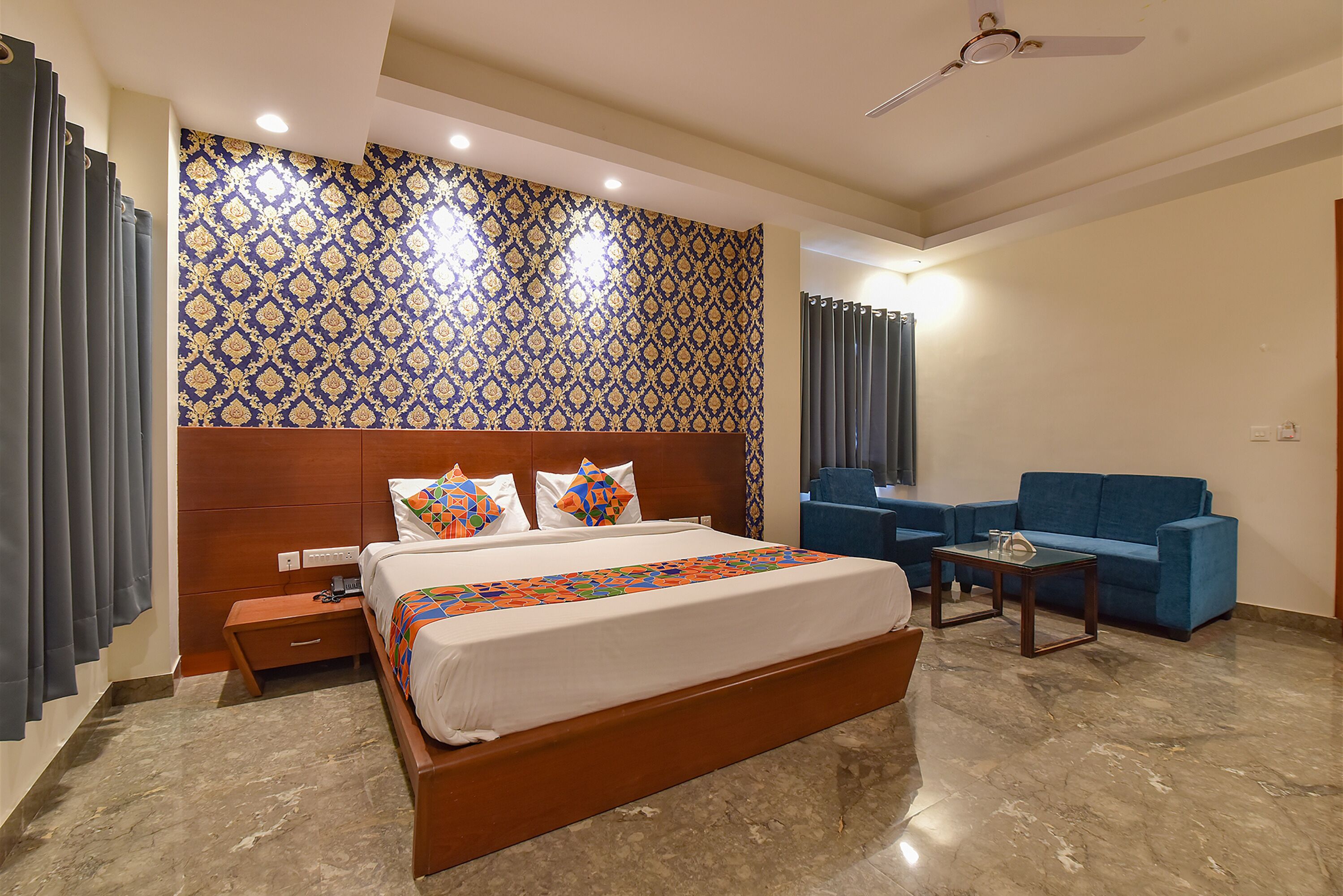 A hotel room with a large bed, a blue sofa, a small table, and a patterned wall.