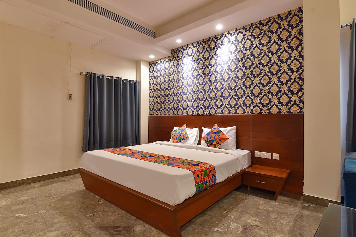 Habitación de hotel con una cama grande, cabecera de madera, mesita de noche y un papel tapiz estampado.
