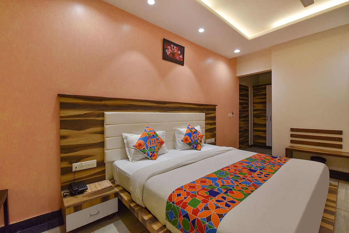 Una habitación de hotel moderna con una cama grande, cabecera de madera y una mesita de noche con teléfono y regleta de enchufes.