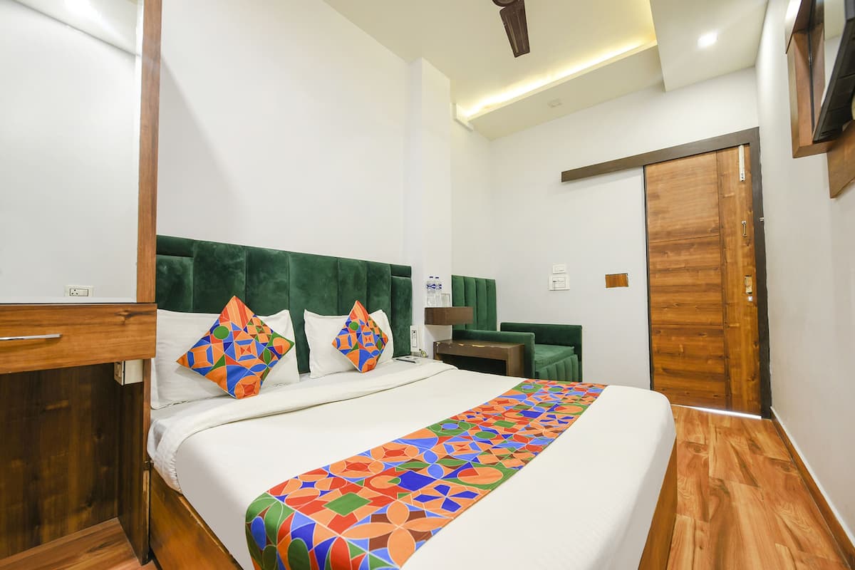 Quarto de hotel com uma cama grande, cabeceira verde, guarda-roupa de madeira e porta de madeira.