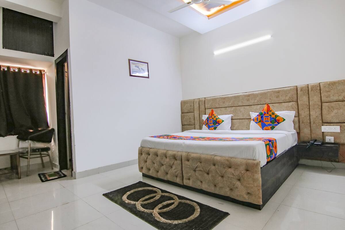 A bedroom with a tufted headboard, a bed with colorful pillows, a bedside table with a phone, and a small rug with circular patterns.