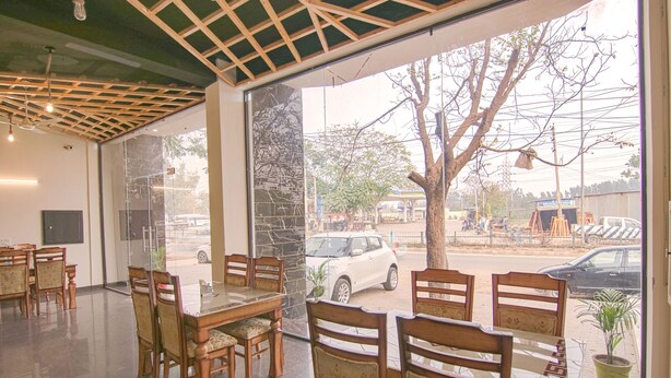 A restaurant with wooden tables and chairs, large windows, and a view of the street outside. - Fabhotel The Nation (Mohali)