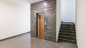 A hallway with a marble wall, a wooden elevator door, and a staircase. - Fabhotel The Nation (Mohali)