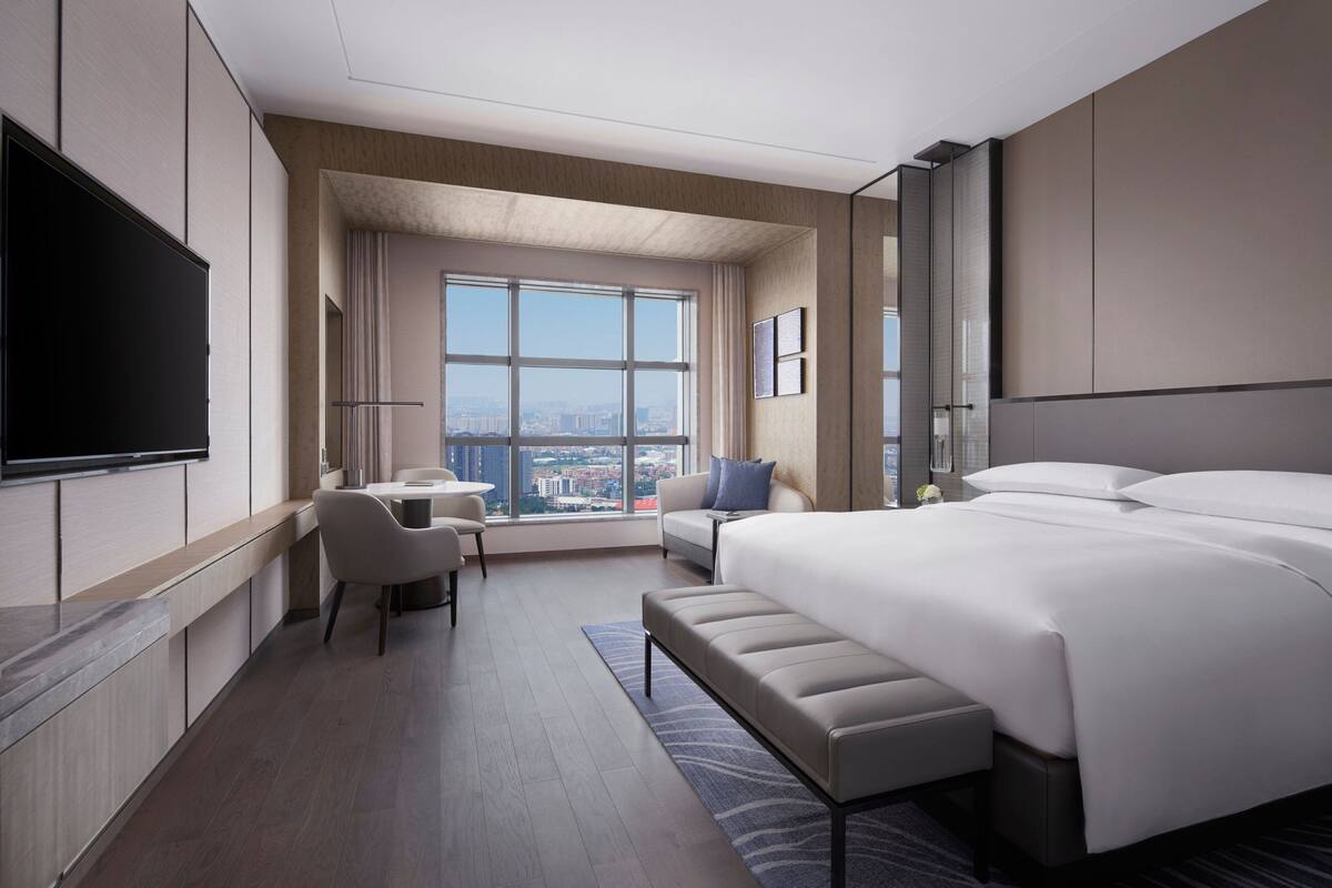 Quarto de hotel moderno com uma cama grande, uma escrivaninha, uma cadeira e uma televisão.