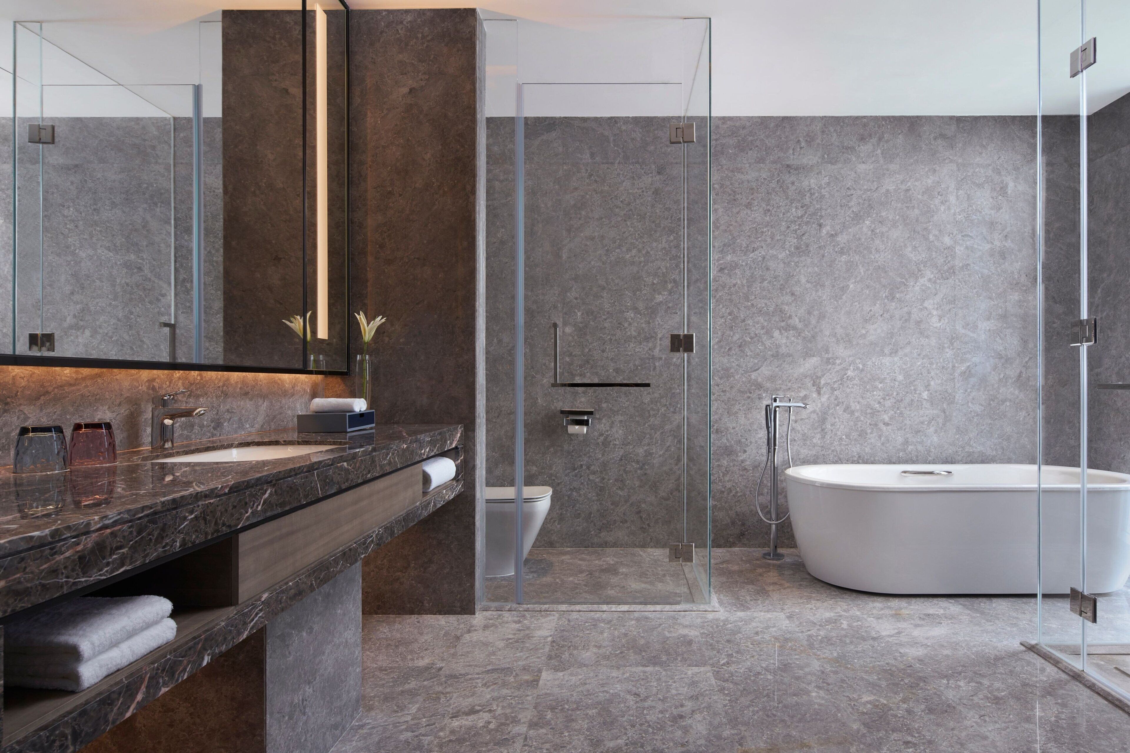 A modern bathroom with a marble countertop, a large mirror, a glass-enclosed shower, and a freestanding bathtub.