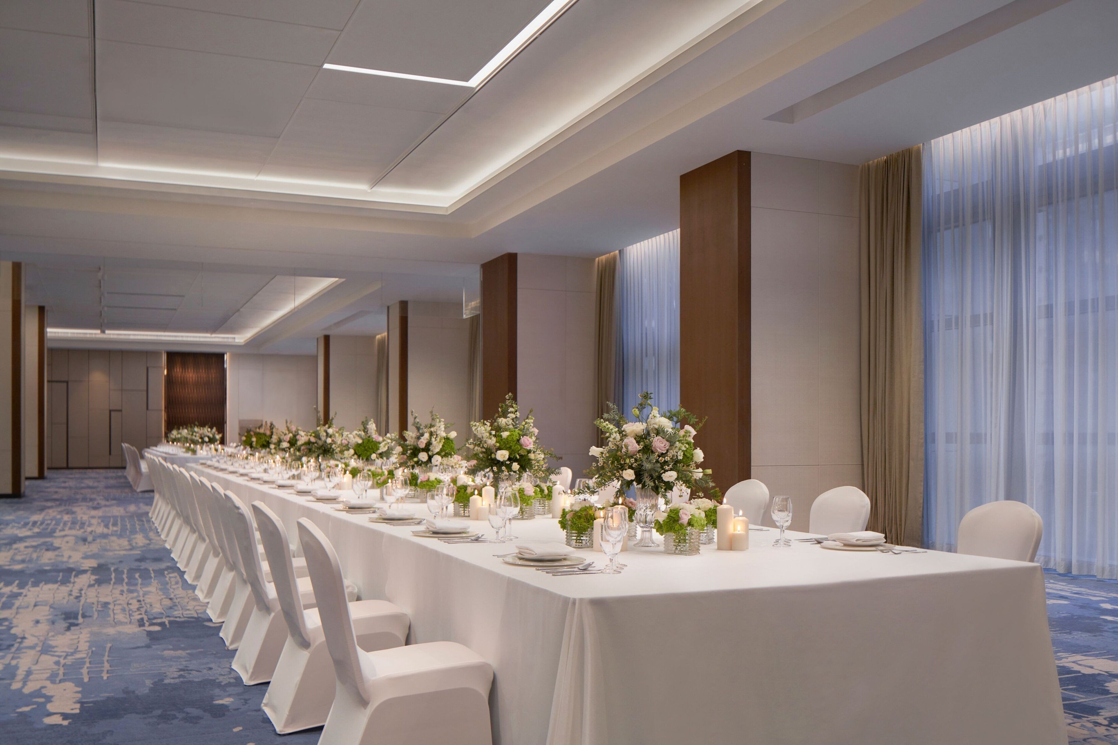 Una larga mesa de banquete dispuesta con sillas blancas, centros de mesa florales y velas.