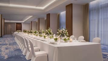 A long banquet table set with white chairs, floral centerpieces, and candles.
