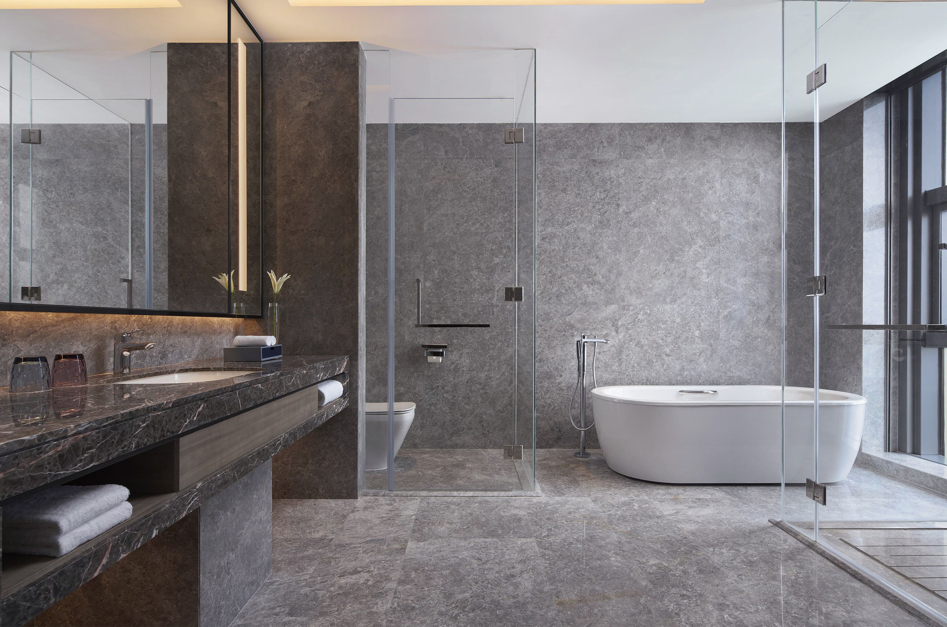 Un baño moderno con ducha envuelta en vidrio, una bañera independiente y encimera de mármol.