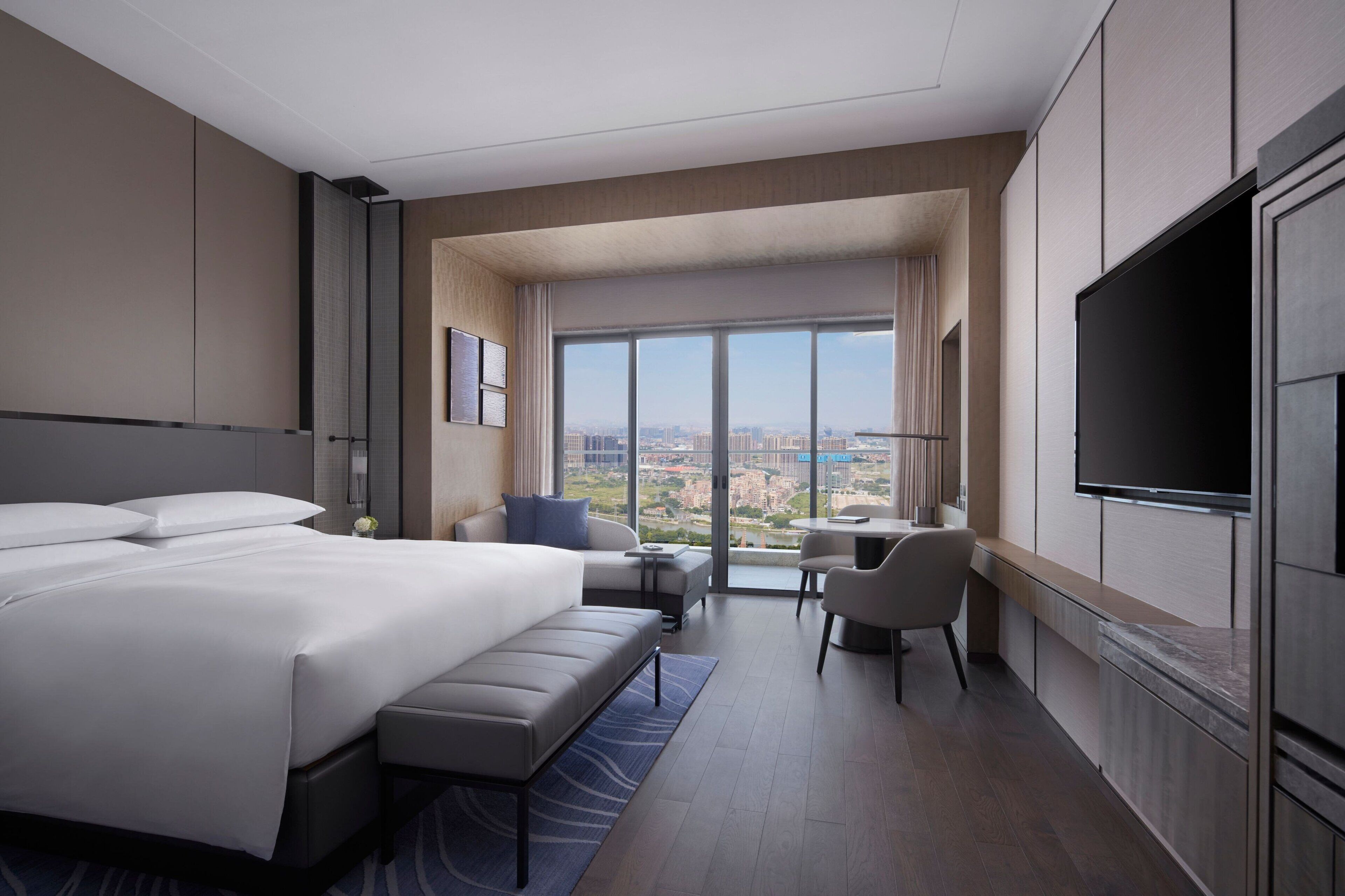 A modern hotel room with a large bed, a desk, a chair, and a TV.