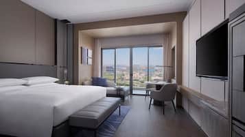 A modern hotel room with a large bed, a desk, a chair, and a TV.