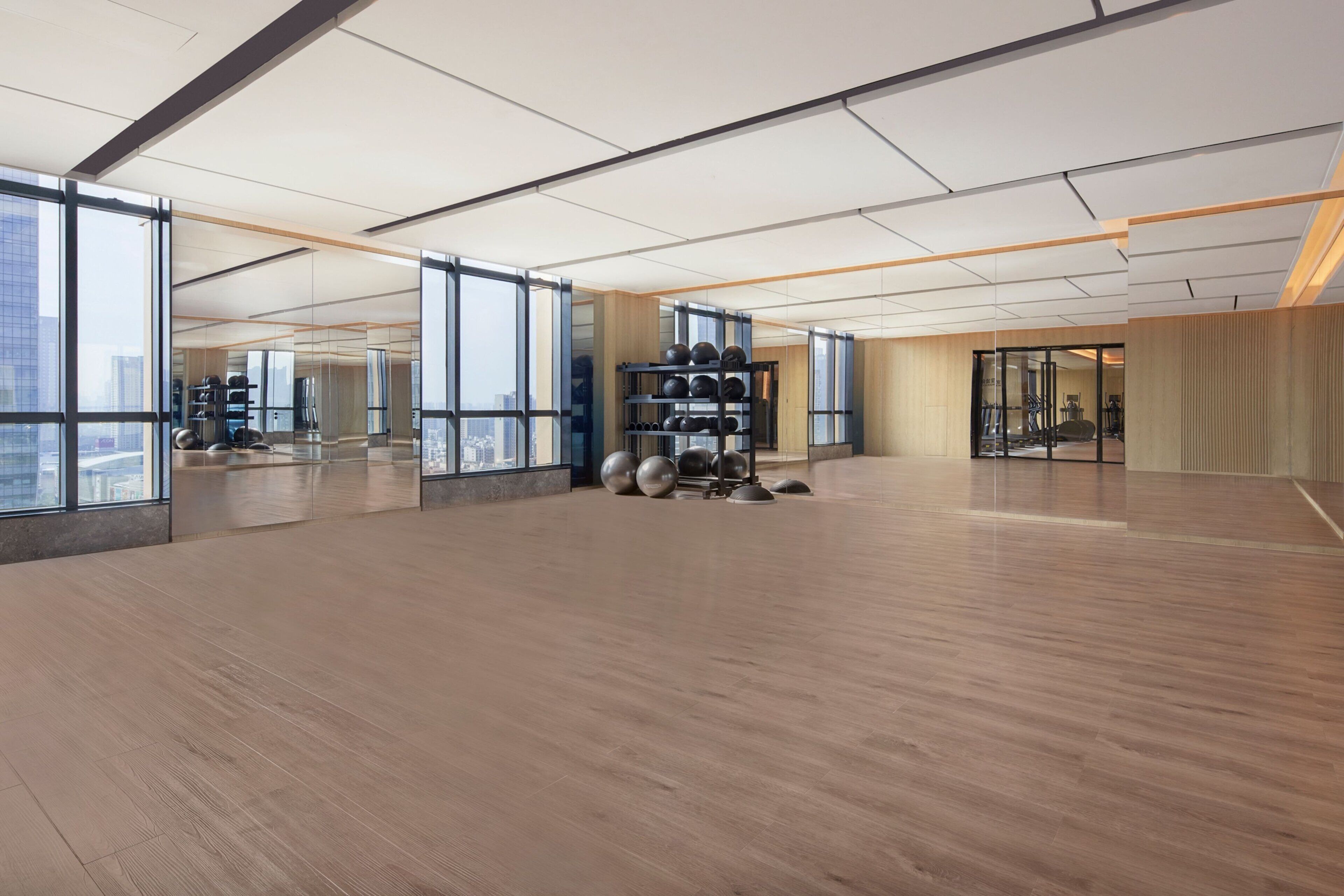 Un gimnasio amplio y moderno con ventanas grandes, suelo de madera y equipamiento de ejercicio.