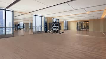 Un gimnasio amplio y moderno con ventanas grandes, suelo de madera y equipamiento de ejercicio.