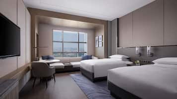 A modern hotel room with a large window, two beds, a flat-screen TV, a seating area, and a city view.