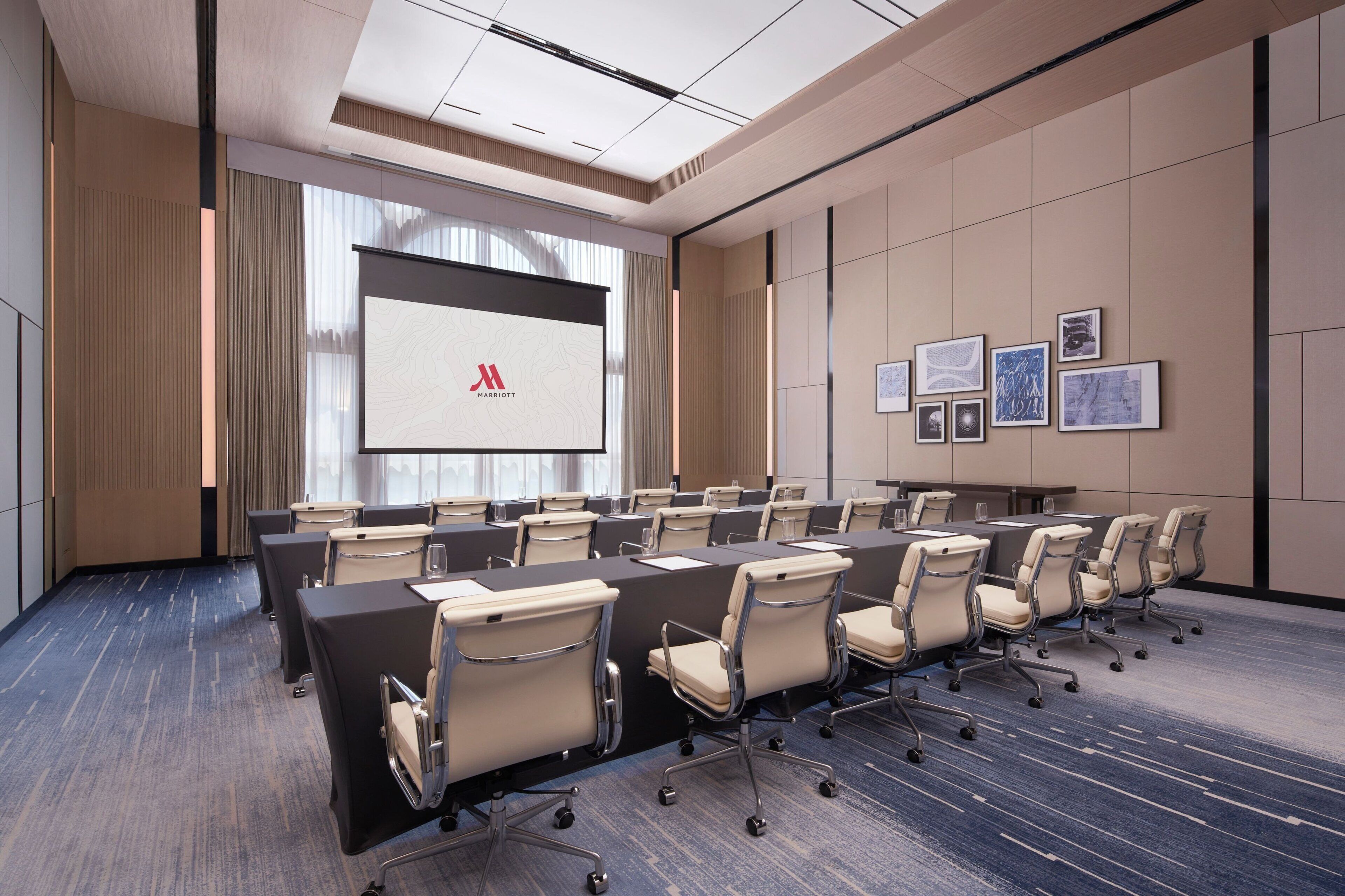 A conference room with a long table, chairs, a projection screen, and framed pictures on the wall.