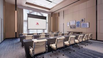A conference room with a long table, chairs, a projection screen, and framed pictures on the wall.