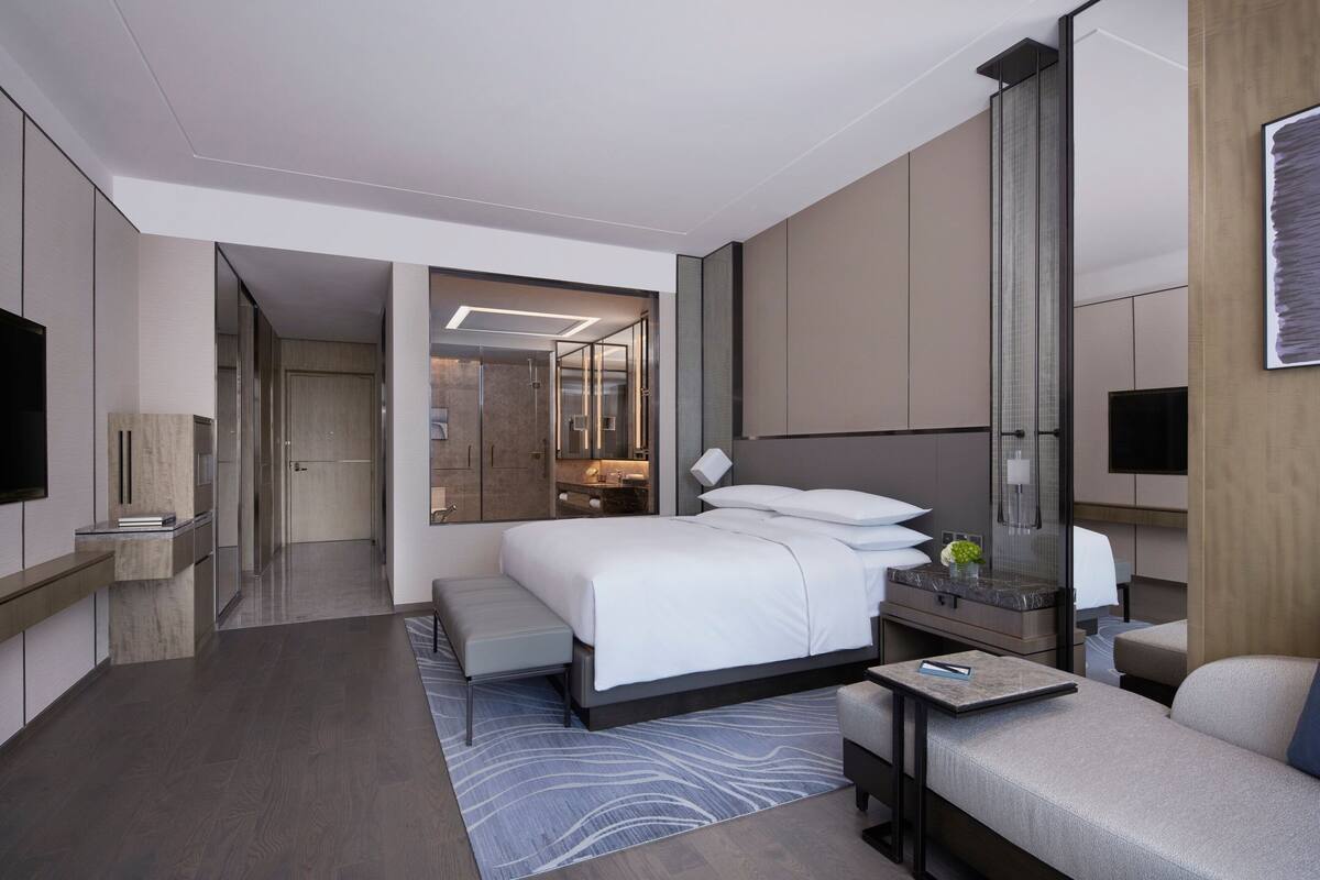 Quarto de hotel moderno com uma cama grande, área de estar, escrivaninha e televisão.