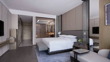 A modern hotel room with a large bed, a seating area, a desk, and a TV.