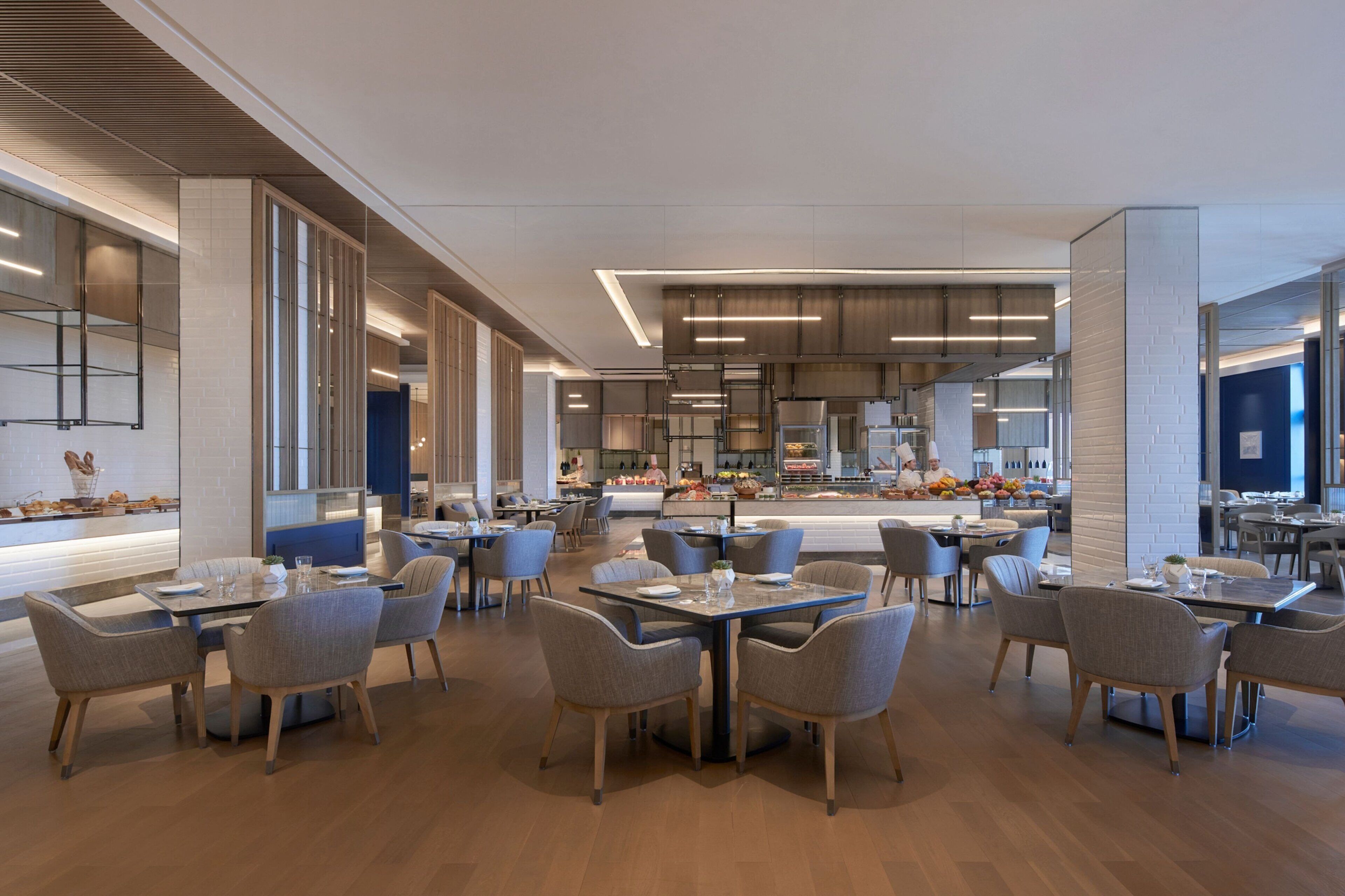 Un comedor moderno con varias mesas y sillas, una zona de cocina central y vistas del espacio para comer.