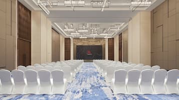 Un salón de conferencias con filas de sillas blancas, una alfombra de diseño azulado y modernos candelabros.
