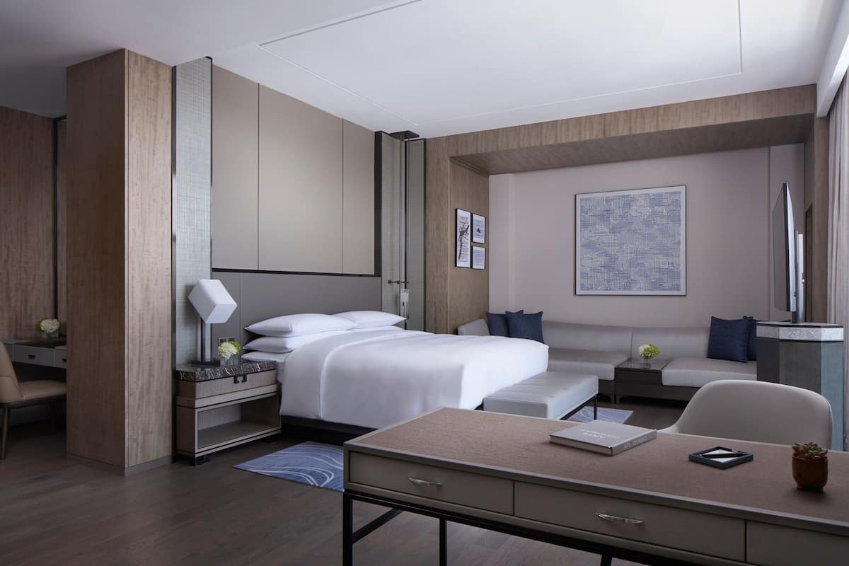 Quarto de hotel moderno com uma cama grande, uma escrivaninha, um sofá e uma televisão.