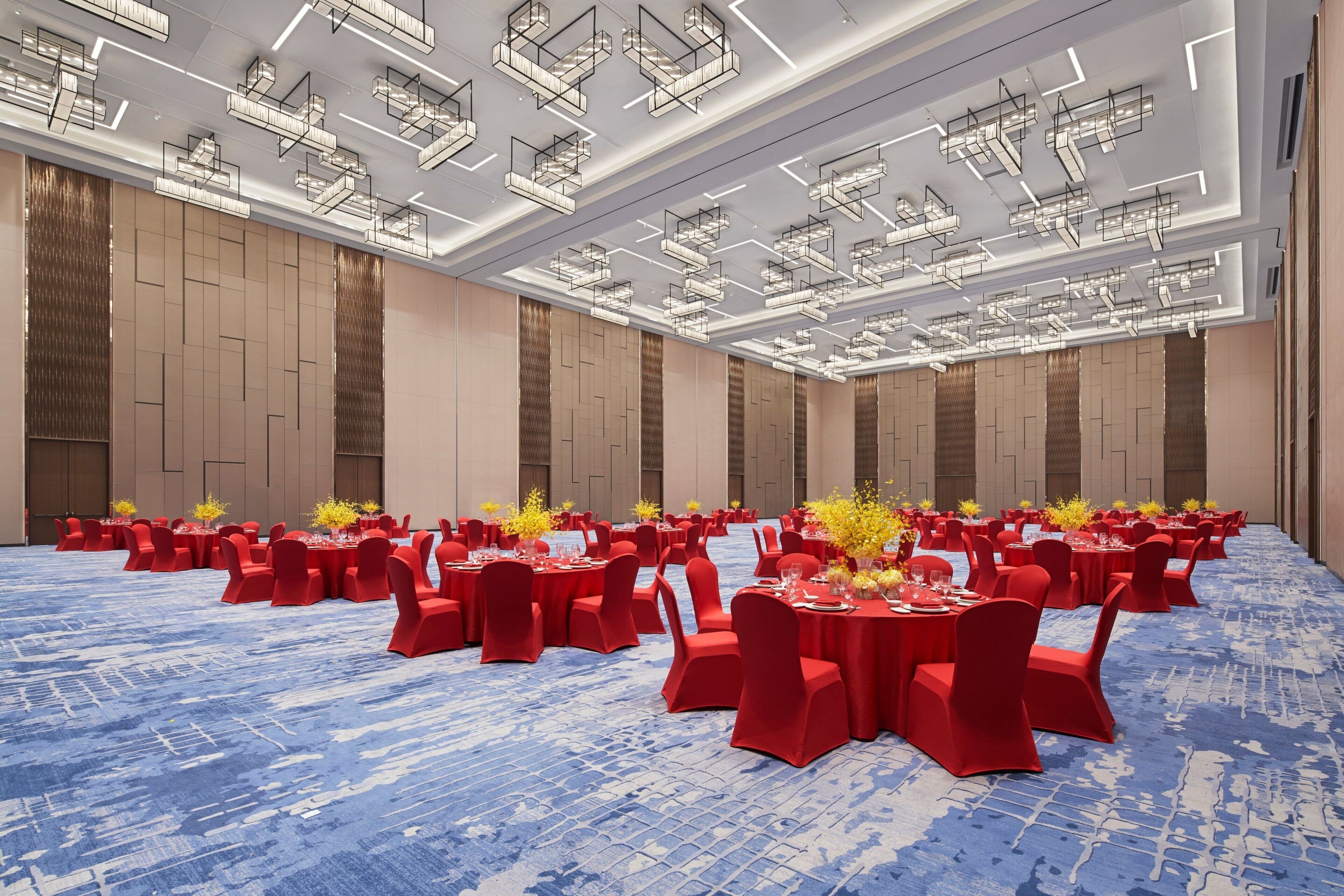 A spacious banquet hall with rows of round tables, red chairs, and modern ceiling lighting.