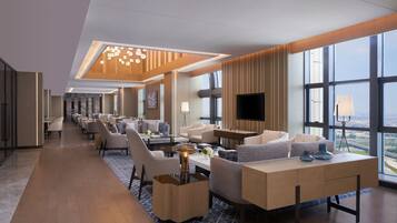 Een moderne hotellobby met een lange receptiebalie, een zithoek en grote ramen met uitzicht op de stad.