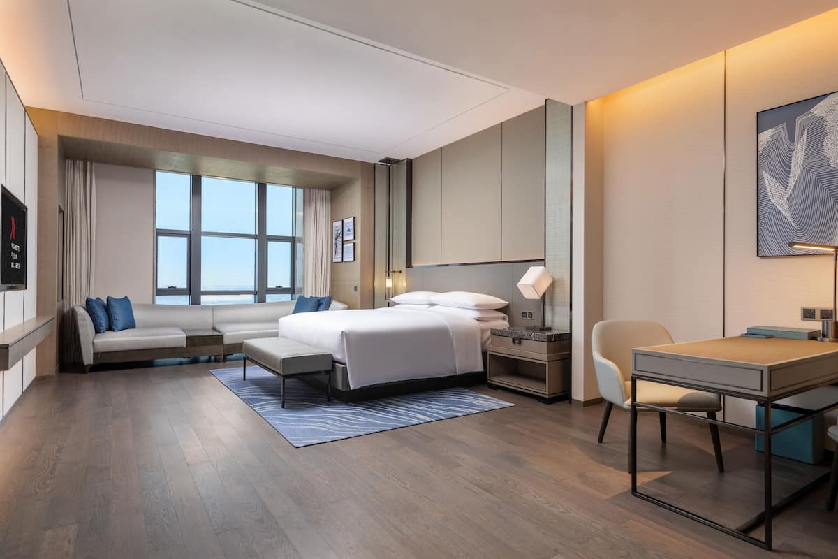 Quarto de hotel moderno com uma cama grande, uma escrivaninha, uma cadeira e vista para a cidade.