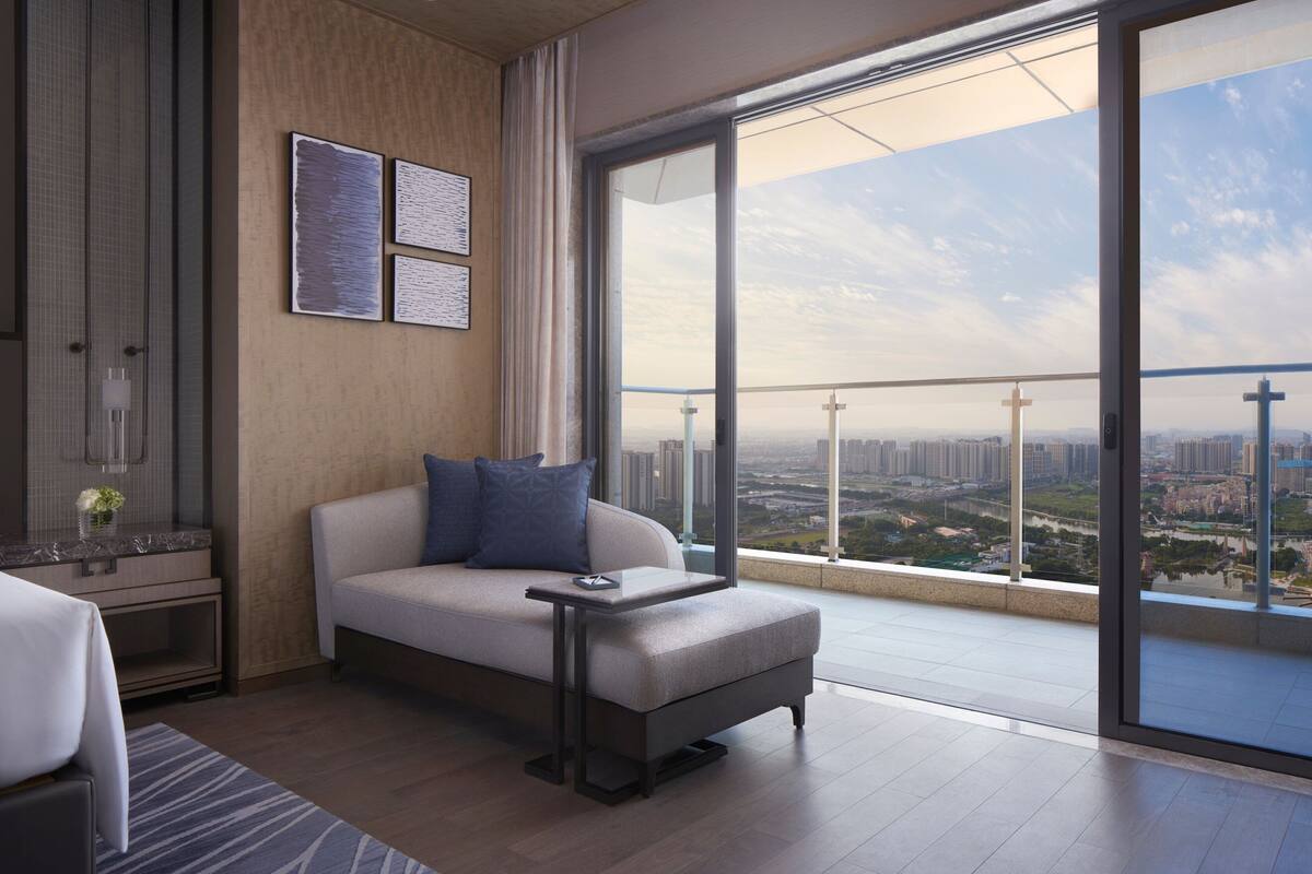 Quarto de hotel moderno com uma varanda grande, um sofá, uma mesinha e vista para a cidade.