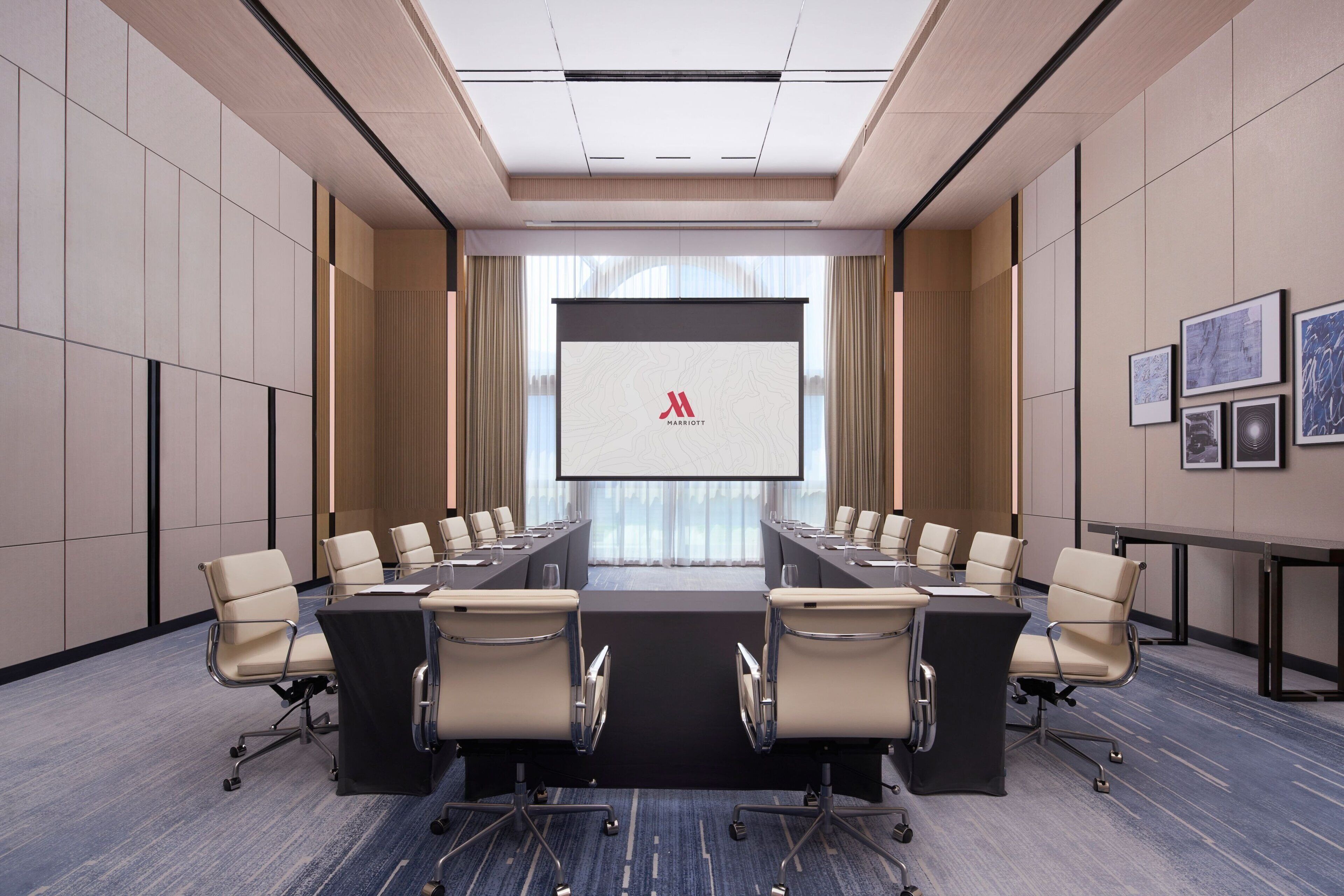 A conference room with a long table, multiple chairs, and a large screen displaying the Marriott logo.