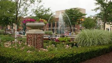 A garden with a fountain, a brick planter with flowers, and a building in the background.