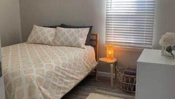 A bedroom with a bed, bedside table, lamp, and a window with blinds.