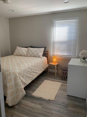 A bedroom with a bed, bedside table, lamp, and a window with blinds. - Perfect for a family of 4 in a village setting! (Canton)