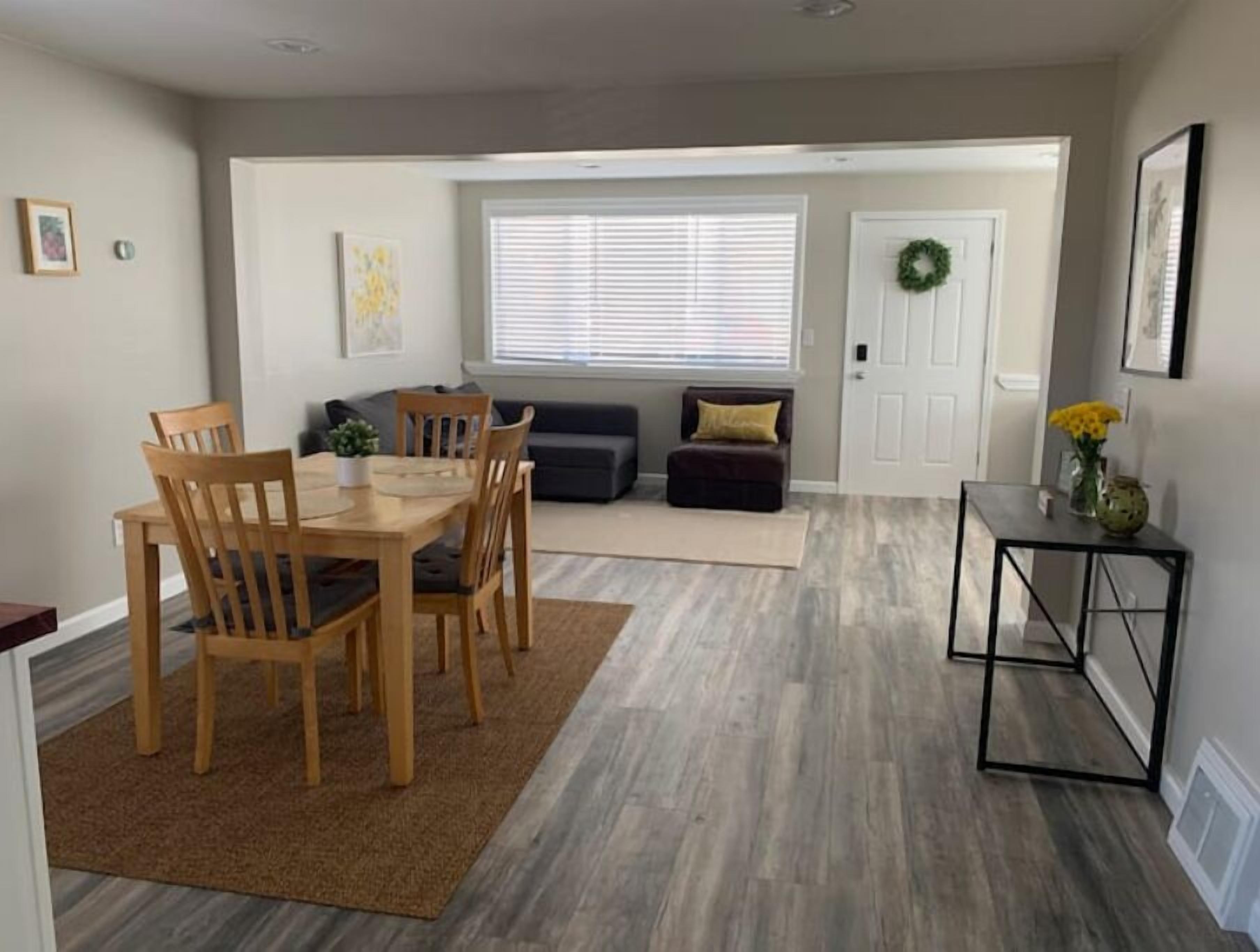 A dining area with a wooden table and chairs, a sofa, and a small side table with a vase of flowers.