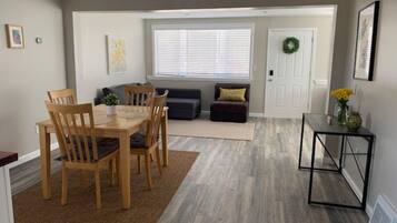 A dining area with a wooden table and chairs, a sofa, and a small side table with a vase of flowers.