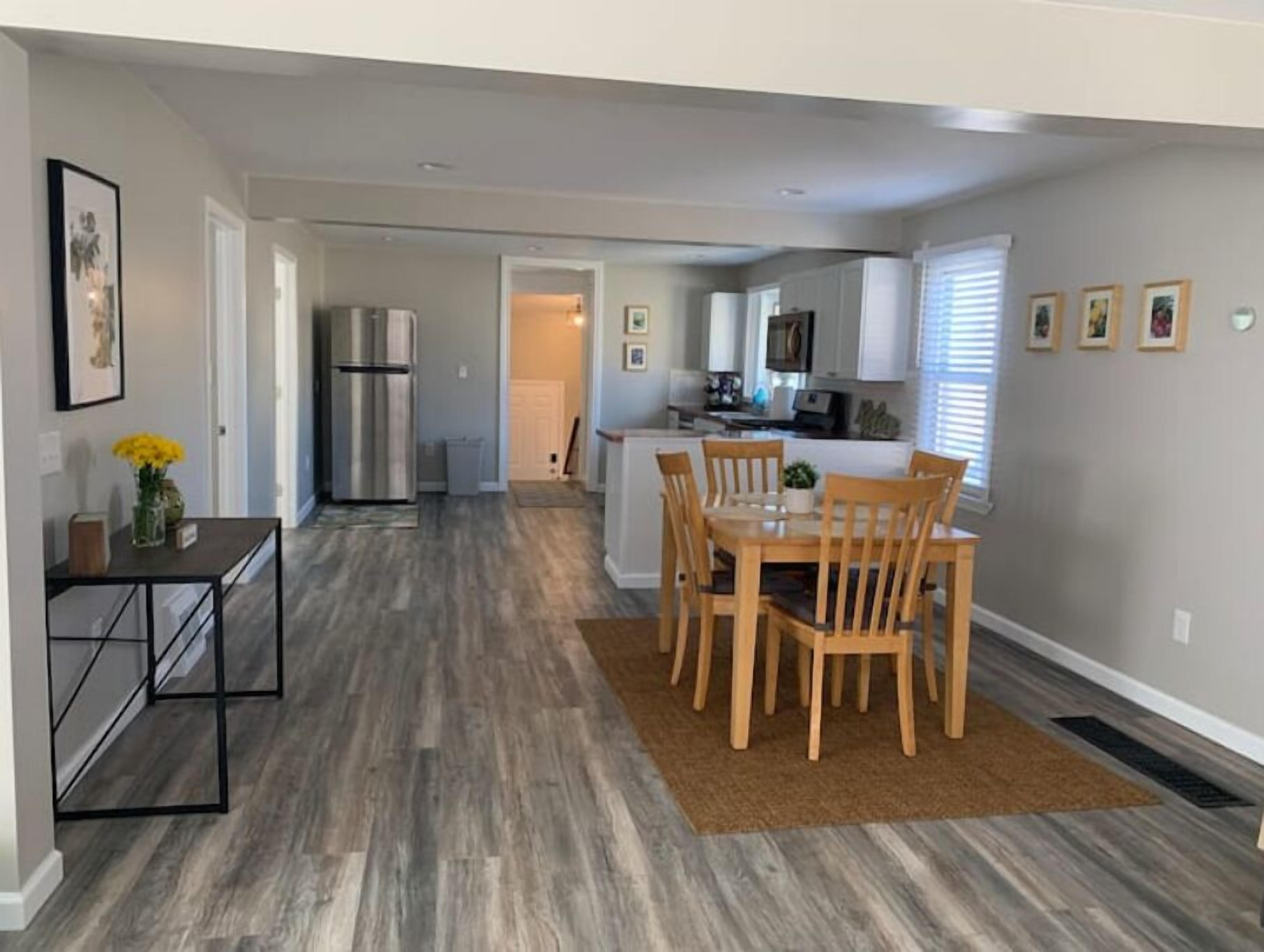 A modern kitchen with white cabinets, a stainless steel refrigerator, and a dining area with wooden chairs and a table.