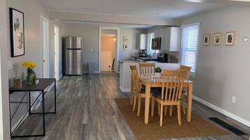 A modern kitchen with white cabinets, a stainless steel refrigerator, and a dining area with wooden chairs and a table.