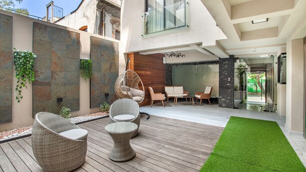 Eine moderne Außenpatio mit Korbmöbeln, einem grünen Kunstturf und einer Glastür, die zu einem Raum mit einer Holzverkleidung und einem Hängesessel führt.