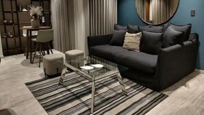Ein modernes Wohnzimmer mit einem dunklen Sofa, einem Glastisch, einem Streifen Teppich und einem runden Spiegel an der Wand.