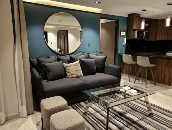 Un salon moderne avec un canapé foncé, une table basse en verre et un grand miroir rond accroché au mur.