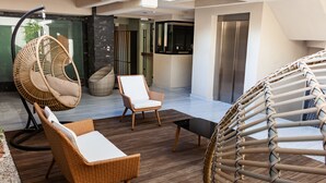 A modern outdoor lounge area with wicker furniture, a hanging chair, and a glass wall.