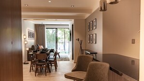 A modern living room with a dining area, featuring a sofa, chairs, a coffee table, and a dining table. There are framed pictures on the wall and a lamp in the corner.