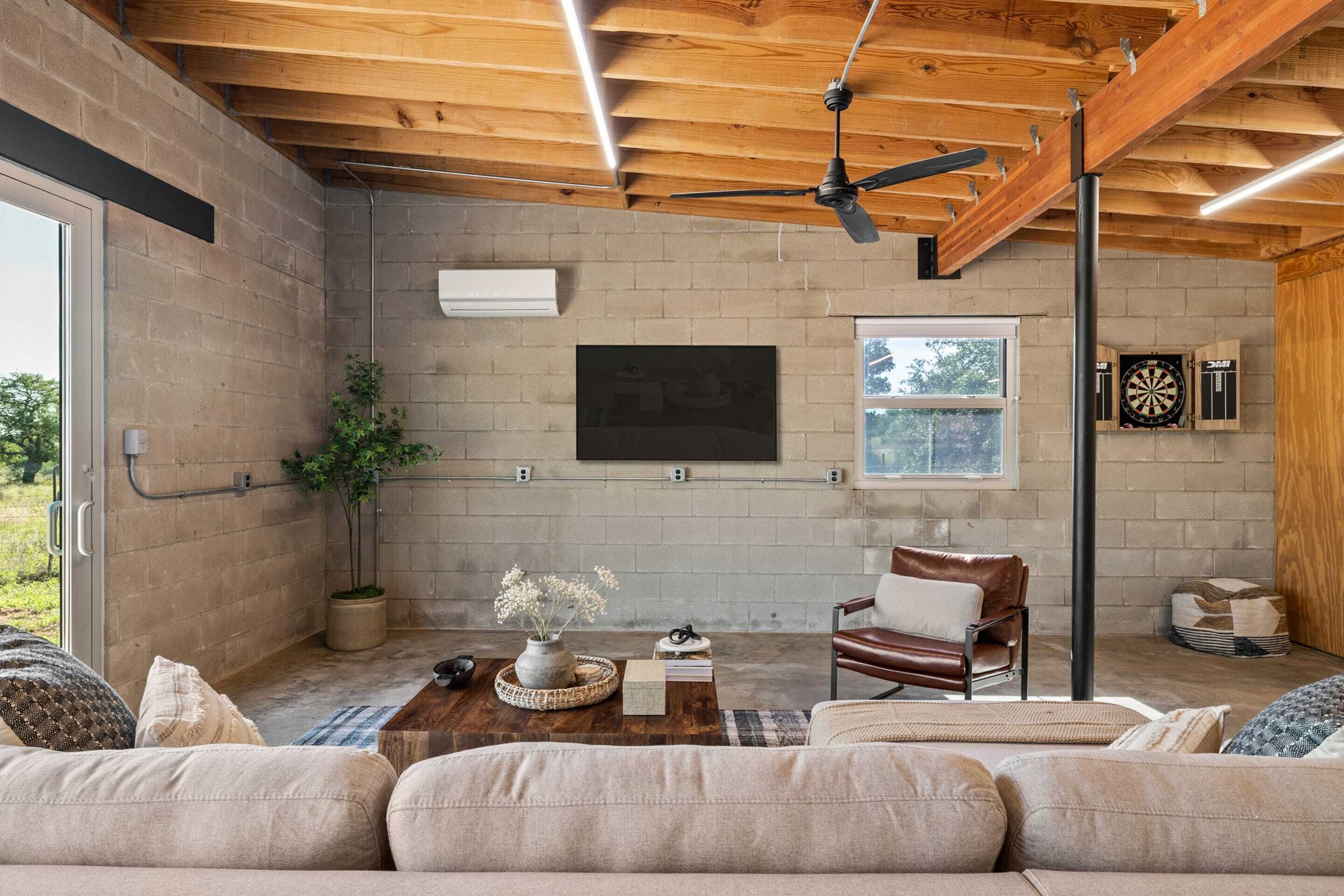 A spacious living area with a wooden ceiling, a mounted TV, a dartboard, and a comfortable seating arrangement.