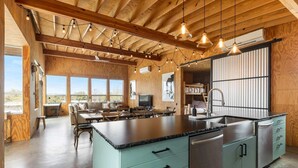 A spacious kitchen with a large island, wooden beams, and pendant lighting. - Luxury Riverfront Retreat | 6 Cabins | Private Pool (Llano)