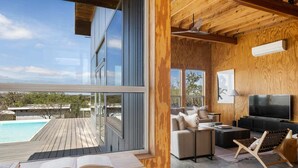 A modern living room with a large TV, comfortable seating, and a view of a swimming pool. - Luxury Riverfront Retreat | 6 Cabins | Private Pool (Llano)