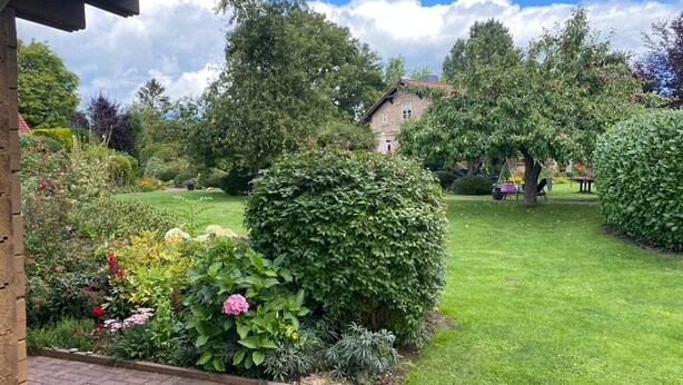 A well-maintained garden with a variety of plants and flowers, a lawn, and a building in the background. - Idyllisches Kleines Blockhaus in Großer Gepflegter Gartenlage (Lutterbek)
