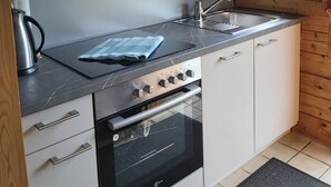 A modern kitchen with a built-in oven, stainless steel sink, and a window with a view of greenery. - Idyllisches Kleines Blockhaus in Großer Gepflegter Gartenlage (Lutterbek)