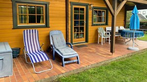 A wooden house with two windows and a covered patio area. - Idyllisches Kleines Blockhaus in Großer Gepflegter Gartenlage (Lutterbek)