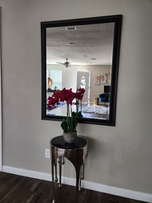 Features a large mirror, a ceiling fan, and a door. Includes a small side table with a potted plant.